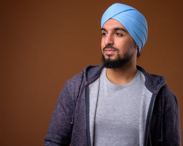 miapelle-mobile-studio-shot-of-young-bearded-indian-man-wearing-casual-clothing-with-blue-turban-against